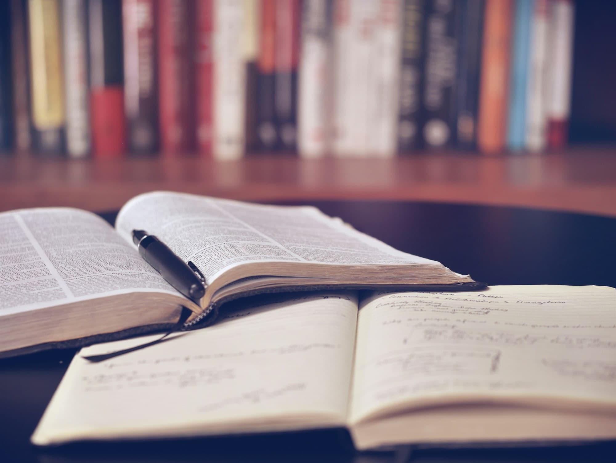 Open books and a notebook with a pen on a library desk