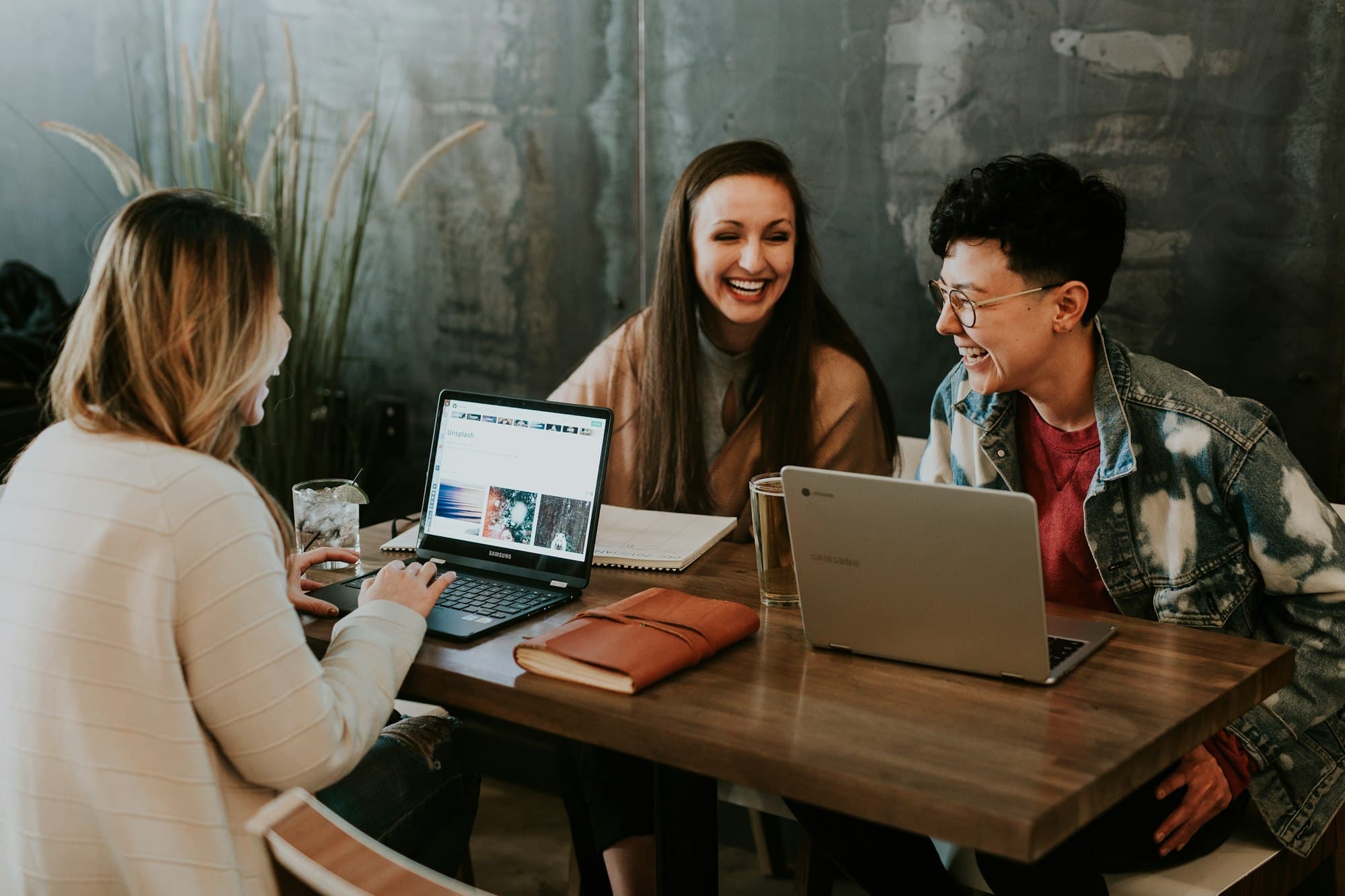 Three friends laughing while studying together at laptops