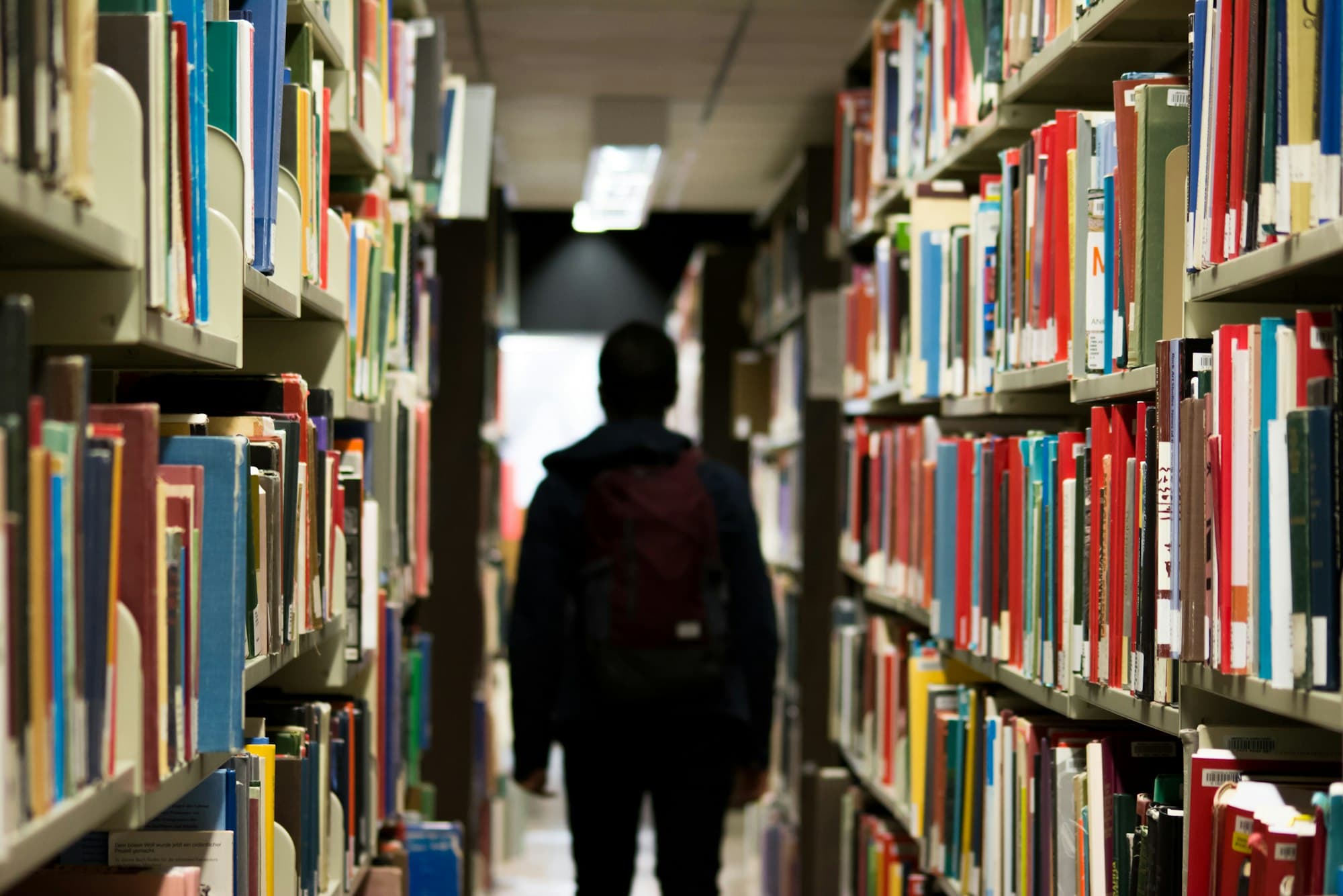 A student walking between tall library shelves